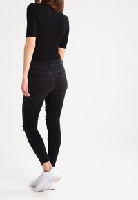 Jeans negros ajustados con cintura alta y detalles desgastados en los costados. Combinados con una blusa negra ajustada y zapatillas blancas.