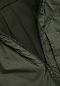 Geopende olijfgroene jas die de zwarte binnenstof en deels zichtbare zwarte rits met stoffen trekkoordjes toont.