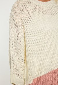 Maglione lavorato a maglia con un design a blocchi di colore crema e corallo, una vestibilità ampia, maniche larghe e un motivo a trama aperta testurizzata.