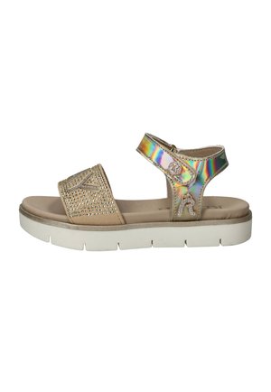 Beige sandaal met witte zool, voorste bandje met kleine studs, iriserend enkelbandje met decoratieve bedeltjes en klittenbandsluiting.