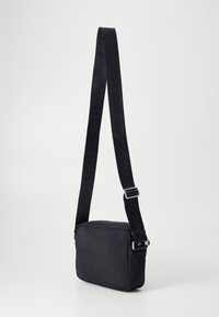 Schwarze Stoff-Crossbody-Tasche mit rechteckiger Form, Reißverschluss und strukturiertem Oberflächenmaterial. Verfügt über einen breiten Tragegurt mit geprägtem Branding.