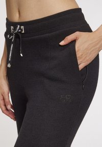 Schwarze gerippte Sweatpants mit einem Kordelzug, Seitentasche und geprägtem "FC 1972" Logo am Oberschenkel. Weiche Textur.