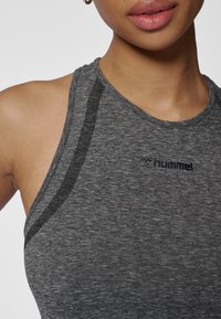 Szary sportowy tank top o dopasowanym kroju, z fakturowaną tkaniną i czarnymi akcentami wzdłuż dekoltu. Posiada logo marki 'hummel'.