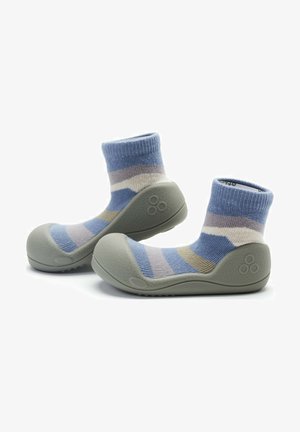 Calcetines suaves a rayas con una combinación de colores en azul claro, gris y beige, adheridos a una suela de goma gris con superficie texturizada y punta redondeada.