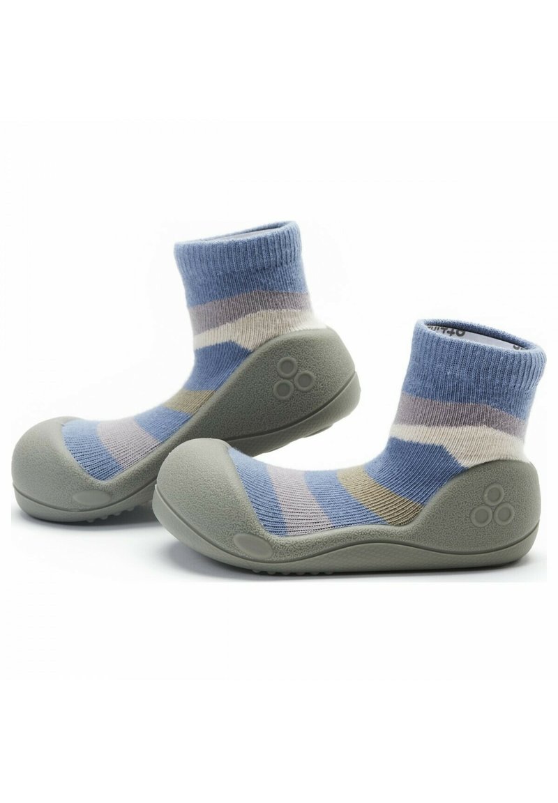 Calcetines suaves a rayas con una combinación de colores en azul claro, gris y beige, adheridos a una suela de goma gris con superficie texturizada y punta redondeada.