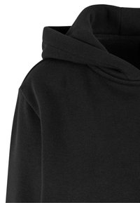 Felpa nera con un tessuto morbido e strutturato. Presenta un ampio cappuccio a doppio strato e una vestibilità rilassata. I dettagli delle cuciture sono visibili lungo le spalle.