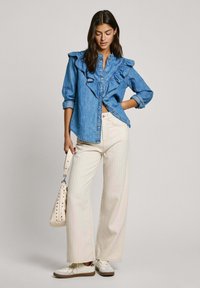 Camisa de denim con cuello rizado y botones, combinada con pantalones de pierna ancha de rayas claras y zapatillas blancas. El bolso tiene acentos de tachuelas.