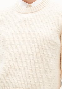 Sweter w kremowym kolorze, dziany z fakturowanym wzorem, z prążkowanym dekoltem i gładkim wykończeniem. Cechuje się luźnym, swobodnym krojem i brakiem widocznych elementów metalowych.