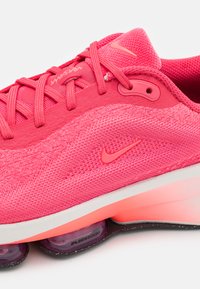 Nike futócipő élénk rózsaszín hálóból, texturált felsőrésszel, párnázott bokarészes kialakítással és átlátszó lila látható Air Zoom párnázással.
