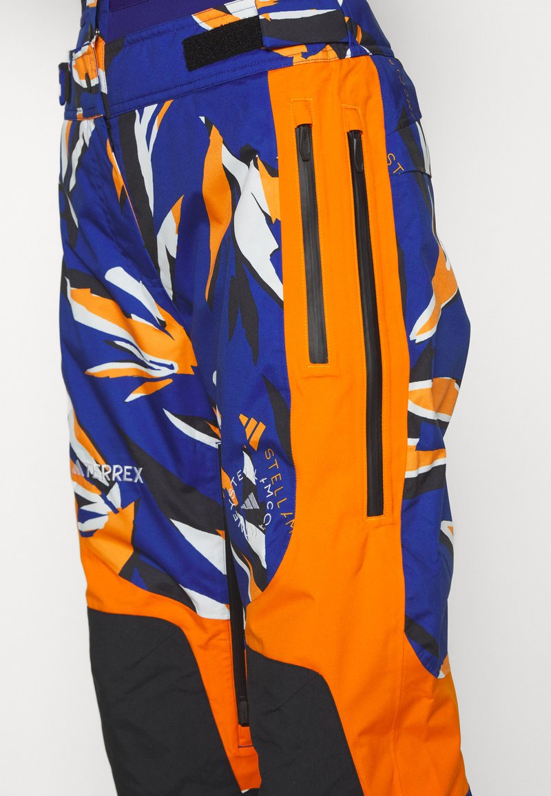 Pantaloni da sci blu e arancioni a fantasia con design aderente, dotati di tasche con zip e accenti neri. Realizzati in materiale resistente e impermeabile.