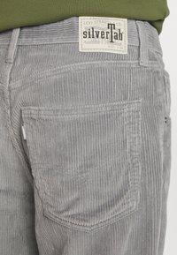 Close-up van een grijze corduroy broekzak met het Levi Strauss silverTab-label en een groene shirt die in de taille is gestopt.