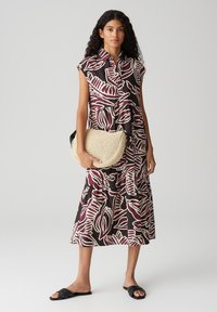 Vestito di tessuto con base nera caratterizzato da ampie fantasie di foglie bianche e bordeaux, con chiusura a bottoni e gonna fluida. Abbinato a una borsa intrecciata.