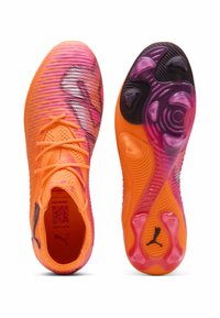 Scarpe da calcio arancioni brillanti con tomaia texturizzata, decorata con accenti rosa e viola. La suola presenta distintivi tacchetti rotondi e triangolari per una migliore aderenza.