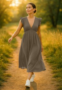 Robe maxi grise à manches courtes avec un décolleté en V, taille froncée et ourlet fluide. Associée à des baskets blanches. Fond vert, éclairage doux.