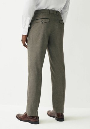 Pantalons à carreaux marron pour hommes, coupe ajustée, avec deux poches arrière. Portés avec des chaussures en cuir marron et une chemise blanche à manches longues.