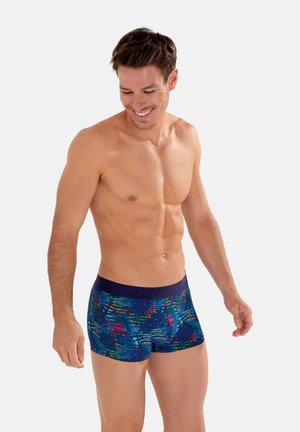 Colorful, patterned trunk-style underwear in a blue base with leafy graphics. Features a solid navy waistband with subtle branding.