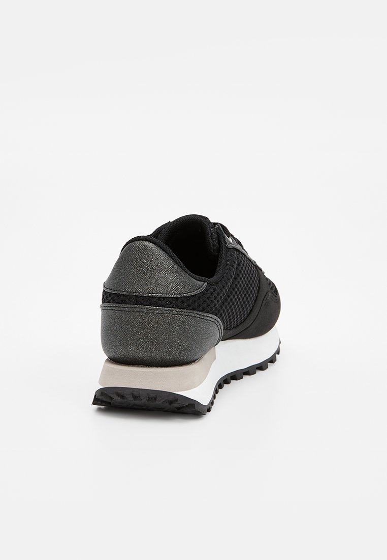 Chaussure de sport noire avec un dessus en mesh, un talon métallique texturé et une semelle intermédiaire blanche. Dispose d'une semelle extérieure en caoutchouc pour l'adhérence.