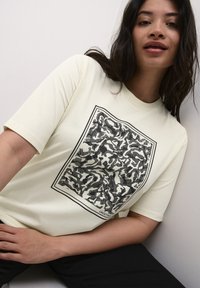Light yellow cotton T-shirt featuring a black sketch pattern in a rectangular frame. Short sleeves and a crew neck design.