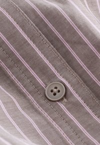 Gros plan d’un tissu rayé marron et rose avec des coutures visibles et un bouton rond marron à quatre trous cousu dessus.