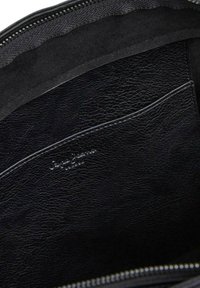 Interno di una borsa in pelle nera, caratterizzato da una superficie texture, chiusura con zip e un piccolo logo impresso sulla tasca.