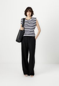 Striped sleeveless top in navy and white cotton; high-waisted black trousers with a relaxed fit; holding a black tote bag.