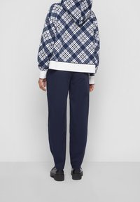 Felpa con cappuccio a scacchi navy con accenti bianchi, dotata di cappuccio con stringhe e polsini a coste. Abbinata a pantaloni navy e scarpe nere.