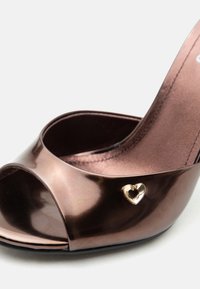 Λαμπερό μπρούτζινο γοβάκι peep-toe με μικρή χρυσή καρδιά ως διακόσμηση στην εξωτερική πλευρά κοντά στο δάχτυλο.