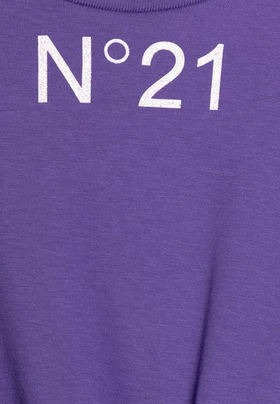 Violetinis audinys su lygiu paviršiumi, ant kurio prie kaklo linijos matyti balti, tekstūruoti „N°21“ užrašai. Paprastas dizainas be papildomų detalių.