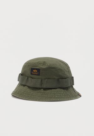 Olívazöld vászonsapka széles karimával és textil szalaggal, az elején egy kis fekete és sárga Alpha Industries logó folttal.