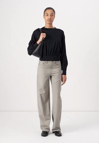 Black long-sleeve top with rounded neckline, paired with light gray wide-leg trousers. Model holds a small black handbag. Smooth texture.