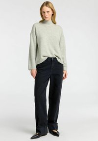 Světle šedý pletený svetr s vysokým krkem, zkombinovaný s tmavě modrými kalhotami širokého střihu. Kalhoty mají volný střih a ohrnuté manžety.