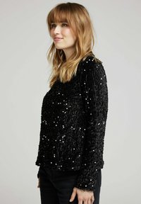 Top noir en sequins avec une surface texturée et pelucheuse et des manches longues. Présente une coupe ample et un col rond, conçu pour un style décontracté.