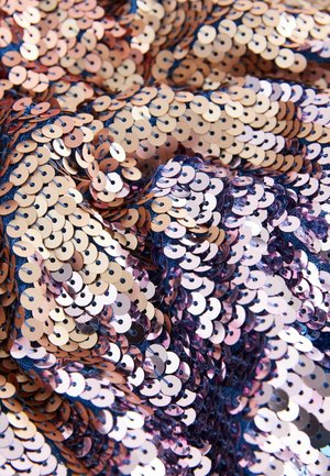 Gros plan sur des sequins superposés dans des tons dorés, cuivrés et bleus, créant un motif texturé et scintillant. La surface semble vibrante et réfléchissante.