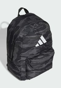 Mochila de camuflaje negra hecha de tela texturizada, con un bolsillo frontal con cremallera y un logo de tres rayas blancas en el lateral.