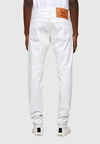 Rear view of person wearing white jeans with leather Diesel brand patch and white sneakers with black stripe and Diesel logo.