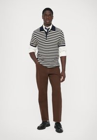 Tumedast ja valgetest triibudest kudum polo särk, millel on krae, kombineeritud pruunide pükste ja mustade kingadega, slim fit disainiga.