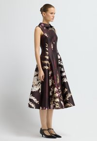 Satinblumenkleid in dunkelburgunderrot mit taillierter Taille und ausgestellt Rock; verfügt über einen klassischen Kragen und eine glatte Textur. Schwarze T-Strap-High Heels.