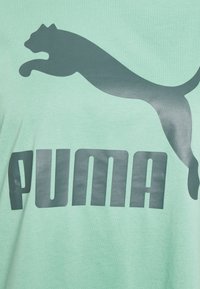 En hoppande puma-logotyp ovanför den feta "PUMA"-texten på en ljusgrön tygbakgrund.