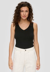 Czarny prążkowany top na ramiączkach z dekoltem w serek, w połączeniu z białymi spodniami na wysoki stan z zapięciem na guzik i kieszeniami z przodu.