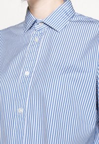 Blue and white striped button-up shirt with a spread collar, featuring a slightly textured fabric and visible buttons along the front.