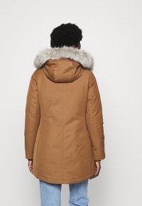 Parka marrone con cappuccio in pelliccia sintetica, dal taglio dritto e polsini a costine, abbinata a jeans azzurri.