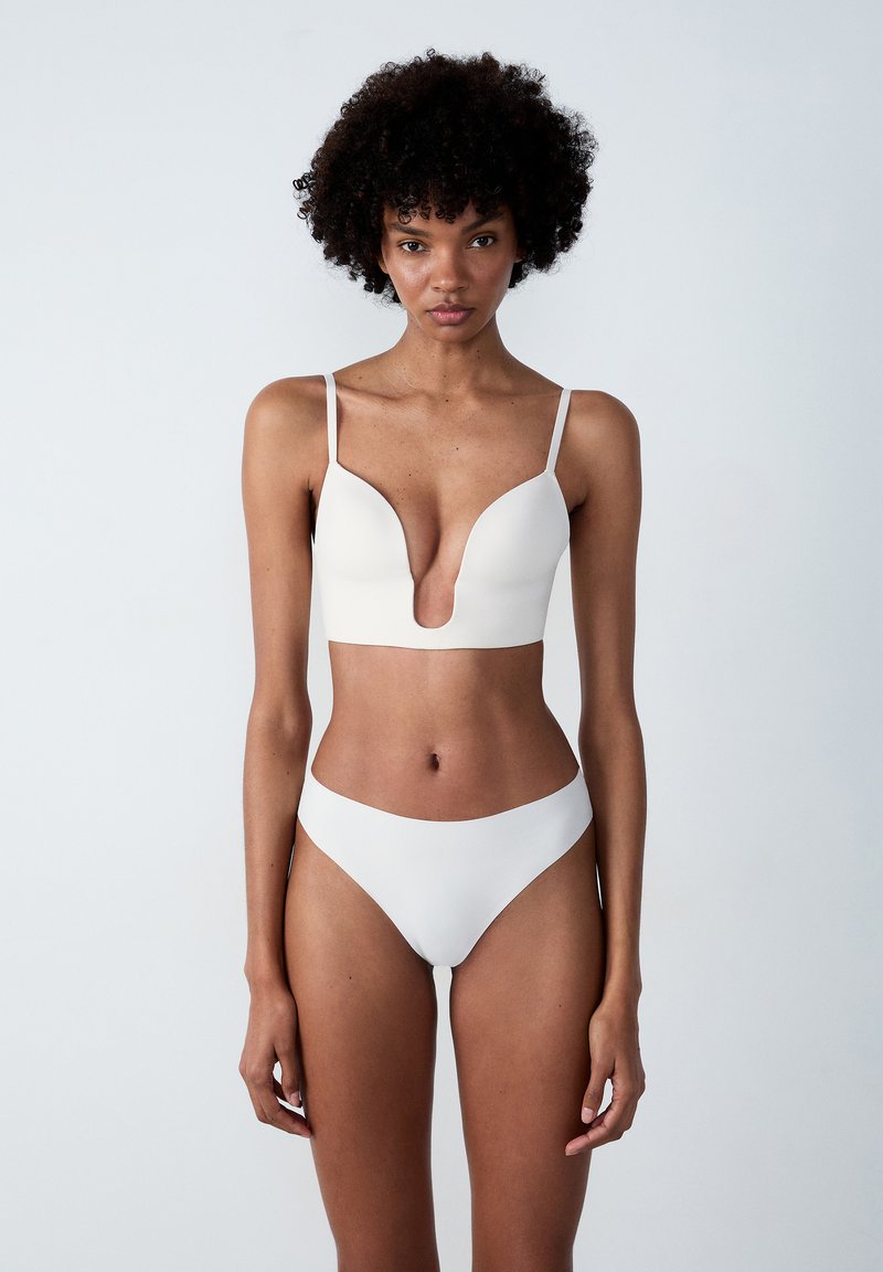 Weißes Bikini-Oberteil mit dünnen Schulterträgern und glatter Textur. Passende tief geschnittene Bikini-Unterteile bieten ein nahtloses Design und minimale Bedeckung.