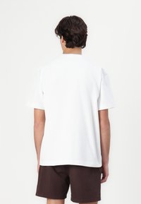 Valkoinen lyhythihainen T-paita, joka on valmistettu puuvillasta ja jossa on rento istuvuus sekä pyöreä kaula-aukko. Sujuva pinta ja yksinkertainen muotoilu, ilman näkyviä logoja.