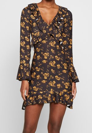 Robe noire à fleurs avec des manches longues, un col froncé et des poignets volantés, ornée de fleurs jaunes, silhouette ajustée et un ourlet à volants évasé.