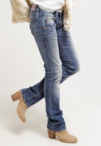 Blå denimjeans med en urtvättad look, lätt slitage, rak benrörelse och bakfickor. Matchat med beige klackstövlar vid anklarna.