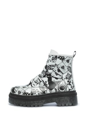 Fekete-fehér bokacsizma fényes felülettel, amelyen játékos dobókocka, szív és pénz szimbólum minták találhatók, vastag, texturált talppal.