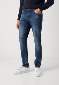 Blå denim jeans med en lige pasform, der har fem lommer, let falmning og syede sømme, sammen med hvide sneakers.