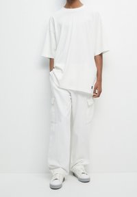 T-shirt blanc surdimensionné et pantalon cargo à jambes larges avec poches latérales. Chaussures : baskets blanches avec accents noirs. Texture du tissu lisse.