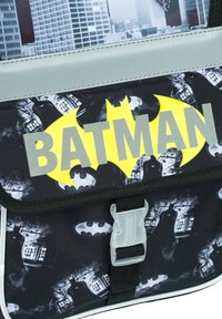 Zaino di tessuto nero con un prominente logo giallo di Batman, dettagli grigi e chiusura a fibbia, decorato con grafiche a tema Batman.