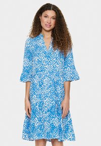 Robe imprimée bleue et blanche avec décolleté en V, manches trois-quarts en cloche, et ourlet évasé, fabriquée à partir d'un tissu léger avec une texture fluide.